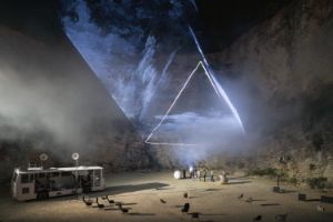 Eine Großaufnahme der Bühne, klein im Vordergrund ein umgebauter Bus, im Hintergrund eine große Neonprojektion von einer Pyramide.
