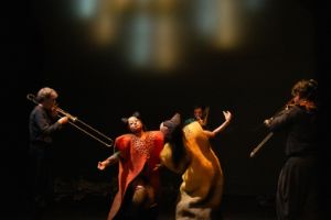 Three trombonists stand around two dancers wearing long felt dresses.