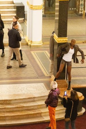 Eine weiblich gelesene Person in kurzer Hose und Blazer, steht auf den Treppenstufen des Lichthofs im Gropius Bau.