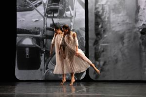 Two dancers in wide dresses and synchronised movement in front of a black and white projection.