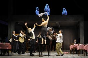 A woman is dancing on a table. A band is playing around her. The scene looks like a situation in a pub.
