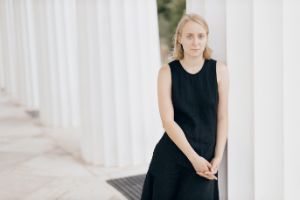 A woman in a black dress stands in front of white columns.