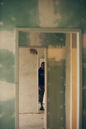 View through three door frames on unpainted walls into several passage rooms, a man is standing in the rear one.