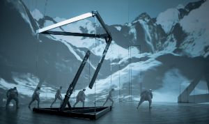 A scene from “Der Zauberberg”; several people are running across a large white stage area with a snowy landscape projected onto the back wall. 