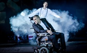 In a scene from “Reich des Todes”, actor Sebastian Blomberg is sitting in an electric wheelchair; with actor Holger Stockhaus standing behind him, swathed in a cloud of fog.