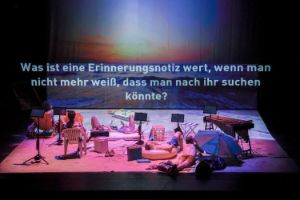 Five people are on stage in a kind of beach scene, above them is written as a projection on a screen “Keine Reaktion aus Australien (No reaction from Australia)”.