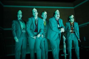 Five actors take off their masks and look into the audience.