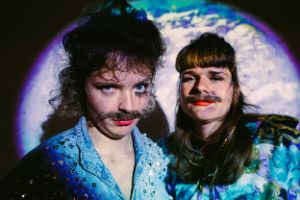 Two female-read persons with moustaches and expressive make-up