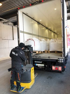 There are several white bags of pink granules in a truck; in front of them is an employee of the Münchner Kammerspiele with a forklift.