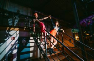 Two people stand on a staircase and clasp their hands over their heads.