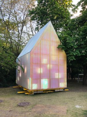 Ein pink leuchtendes Haus steht im Garten des Festspielhauses zwischen blühenden Kastanien.