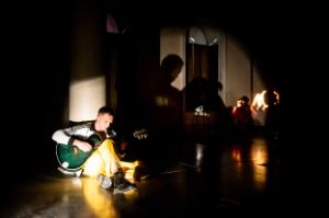 A man plays acoustic guitar on a sparsely lit stage.