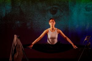 One woman stands confidently between two chairs.