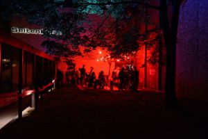A group of people, illuminated by red light, gathers in front of the side stage of the Berliner Festspiele.