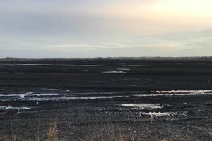 The traces of machines can be seen on a flat earthen landscape with a few puddles.