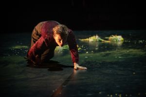 A person in trousers and a velvety top on all fours on a stage