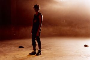 A person in casual clothes on a stage flooded with red light