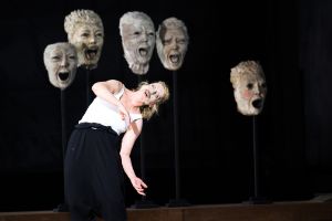 A person with a face mask bends their body in front of five impaled busts