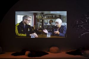 Ein Bildschirm zeigt zwei sich unterhaltende Personen in einem Wohnzimmer