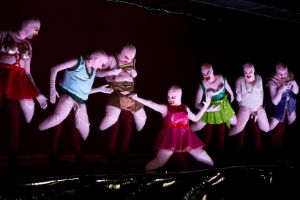 Seven performers in costumes with pink balaclava masks and latex clothing