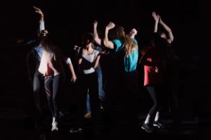A group of young people perform dance movements in the dark.