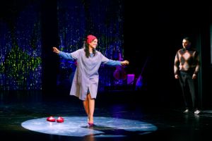 Eine Frau in Arbeitskleidung auf Stöckelschuhen performt im Scheinwerferlicht.