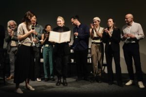 Nora Hertlein-Hull übergibt Regisseurin Luise Voigt die Theatertreffen-Urkunde. Im Hintergrund steht das Ensemble.