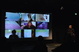 Amitesh Grover steht neben einer Leinwand, auf die ein Zoomvideocall projiziert wird.