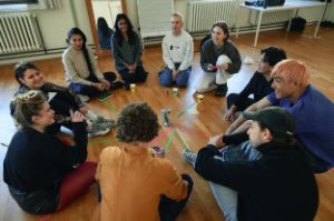 Ein Gruppe von Menschen sitzt in einem Kreis auf dem Boden und unterhält sich.