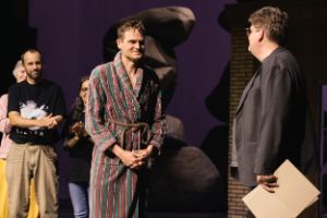Matthias Pees übergibt Fabian Hinrichs die Theatertreffenurkunde. Im Hintergrund steht das Ensemble.