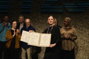 Meryl Tankard zeigt die Theatertreffenurkunde. Im Hintergrund steht das Ensemble.