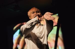 Ein Performer auf der Bühne, der die Hände zur Kamera streckt.