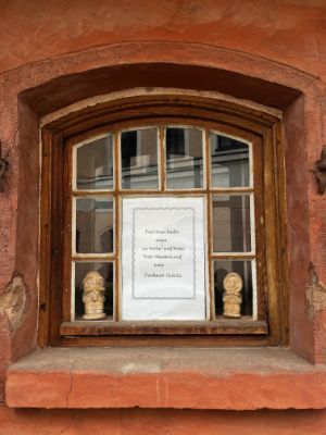 A sign in the window of an ochre-coloured building, surrounded by two wooden statues