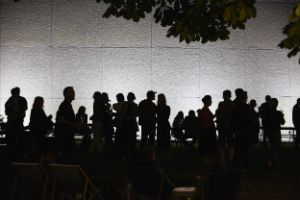 Eine Gruppe von Menschen sitzt abends an Biertischen auf einer Wiese neben einem Gebäude, andere stehen an einem Imbisswagen Schlange.