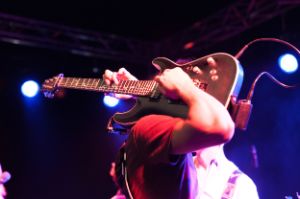 Eine Person spielt auf einer E-Gitarre, die auf der rechten Schulter liegt.