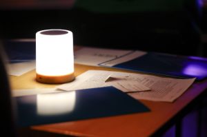Auf einem Tisch mit einer kleinen zylinderförmigen Lampe liegen verschiedene Broschüren und Dokumente. 