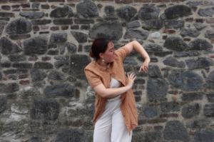 Eine junge Frau vollführt eine tänzerische Bewegung vor einer Steinwand.