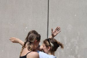 Zwei junge Frauen stehen dicht beieinander und verschränken ihre Arme ineinander.