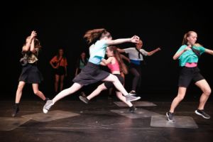 Young dancers jump in wide steps between plastic plates lying on the floor.