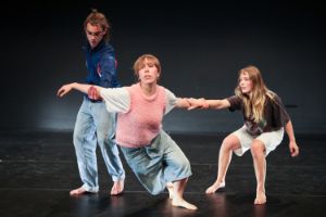 One person drops their centre of gravity forward while two young dancers hold them by the arms.