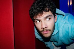 Can-Bastian Paul schaut an einem roten Vorhang vorbeigebeugt über den rechten Bildrand hinaus.