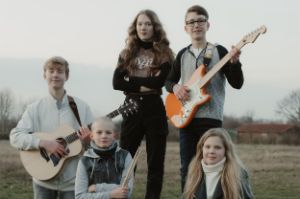 Die fünf Bandmitglieder lächeln sanft in zwei Reihen vor einer Wiese, zum Teil ihre Instrumente haltend.
