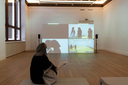 Eine Person Blickt auf eine Leinwand vor sich. Zu sehen sind vier verschiedenen Szenen einer Performance.