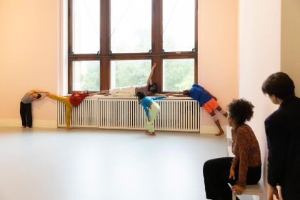 In einem hellrosa gestrichenen Raum findet eine Live-Performance mit dem Titel „study now steady“ statt. Mehrere Tänzer:innen bewegen sich dynamisch durch den Raum und beziehen dabei den Boden, die Wände, die Fenster und die Heizkörper  in ihre Choreografie ein. Das Publikum sitzt auf einfachen Bänken und beobachtet aufmerksam das Geschehen.