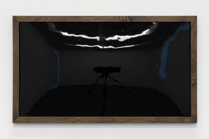 A glossy black rectangle in a dark wooden frame hangs horizontally on a white wall. Its reflective surface faintly mirrors the surrounding space. The artwork is shown from the front.