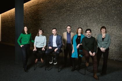 Sieben Personen (Mitglieder der Theatertreffen-Jury 2025) vor einer Kieselwand